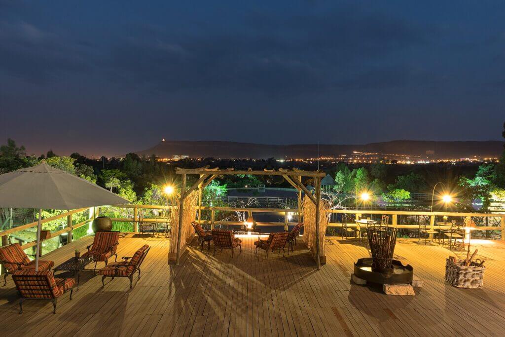 Inviting outdoor patio at night with vibrant lights and comfortable seating, overlooking a cityscape.