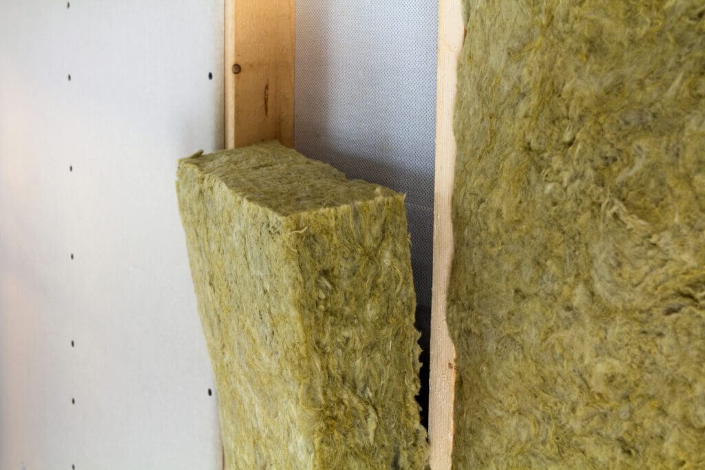 Mineral wool insulation being installed between wooden studs.