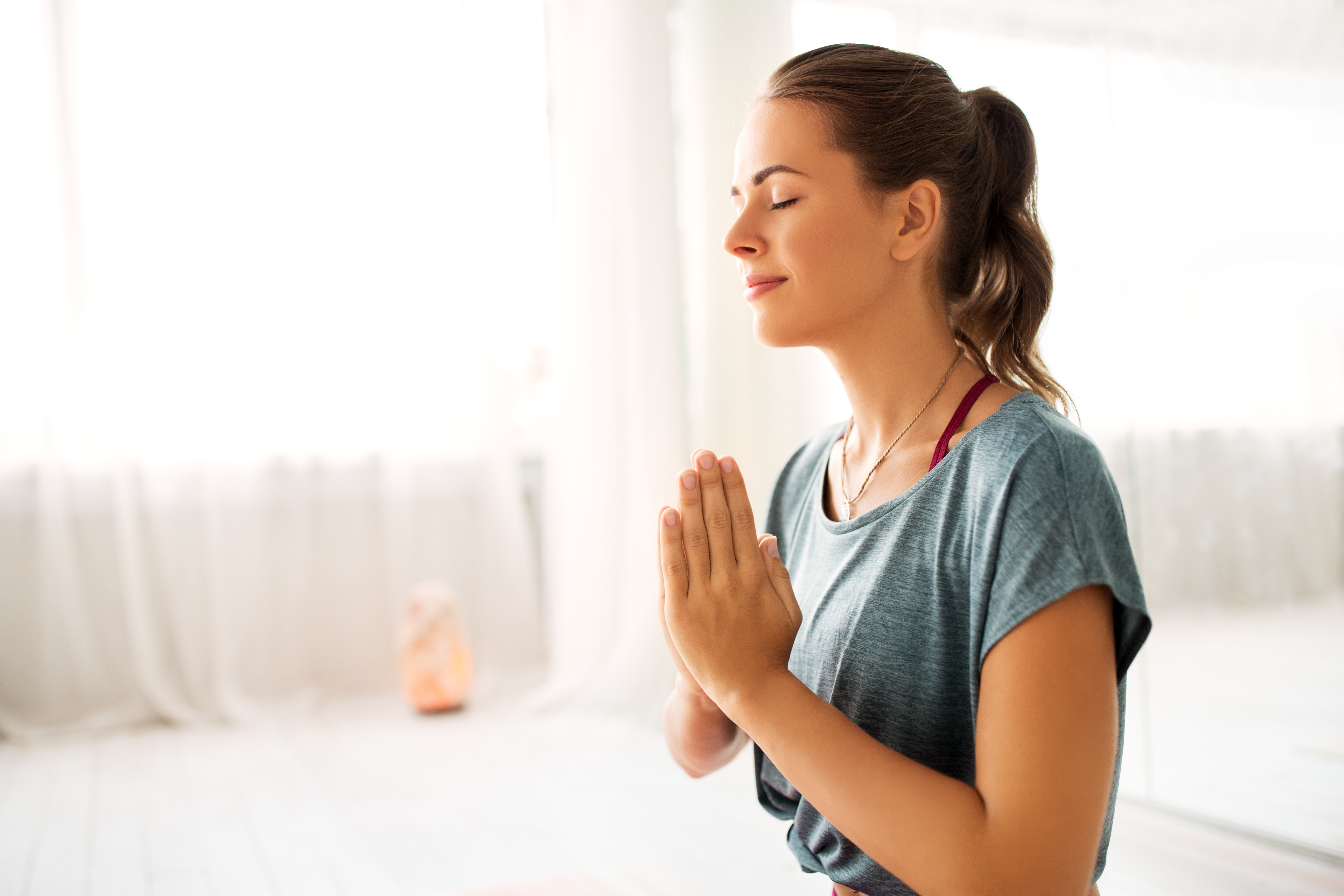 Woman meditating peacefully in a bright, sunlit room, insulated by vinyl windows.