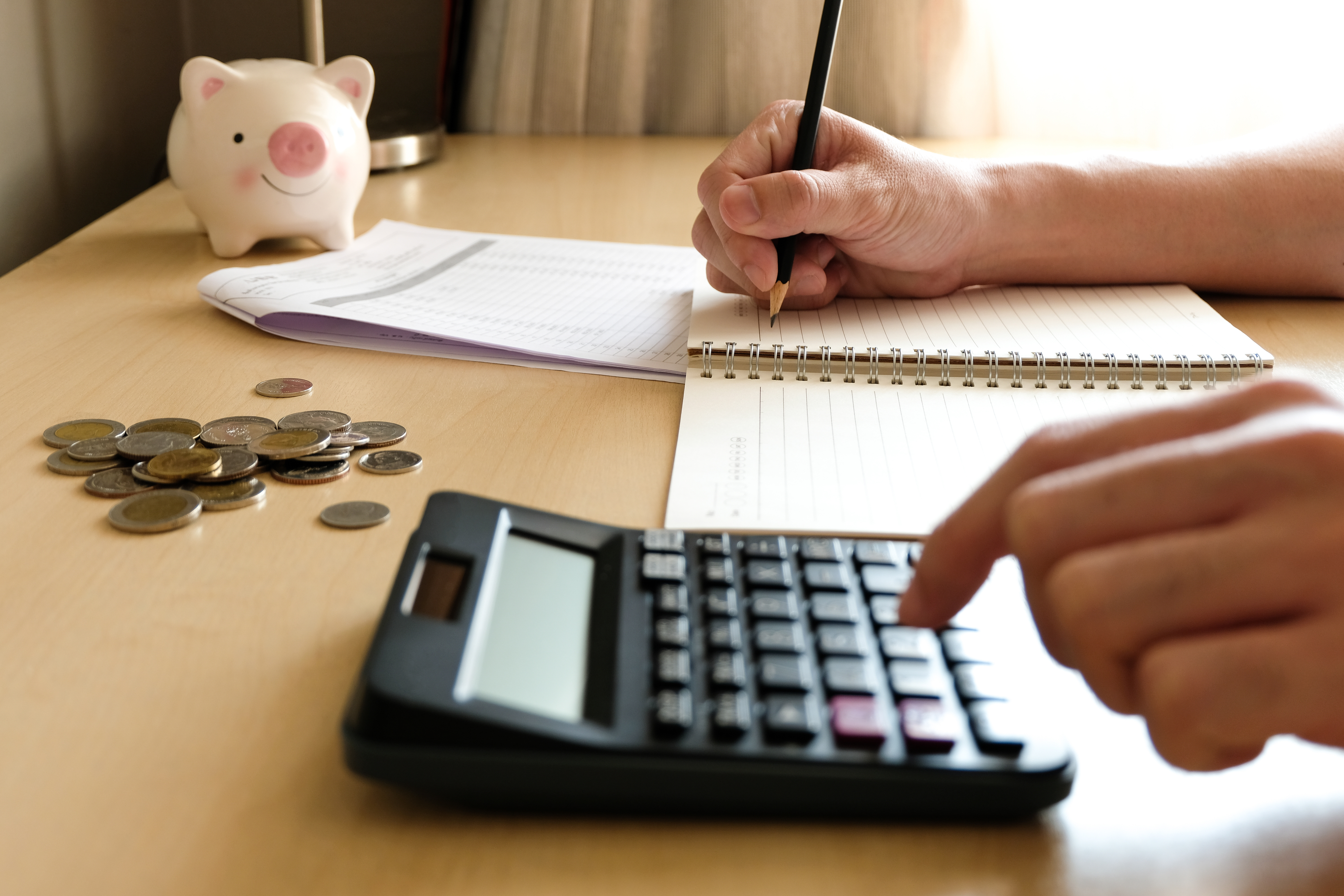 Person calculating home improvement costs with a calculator, notebook, and scattered coins on a desk.