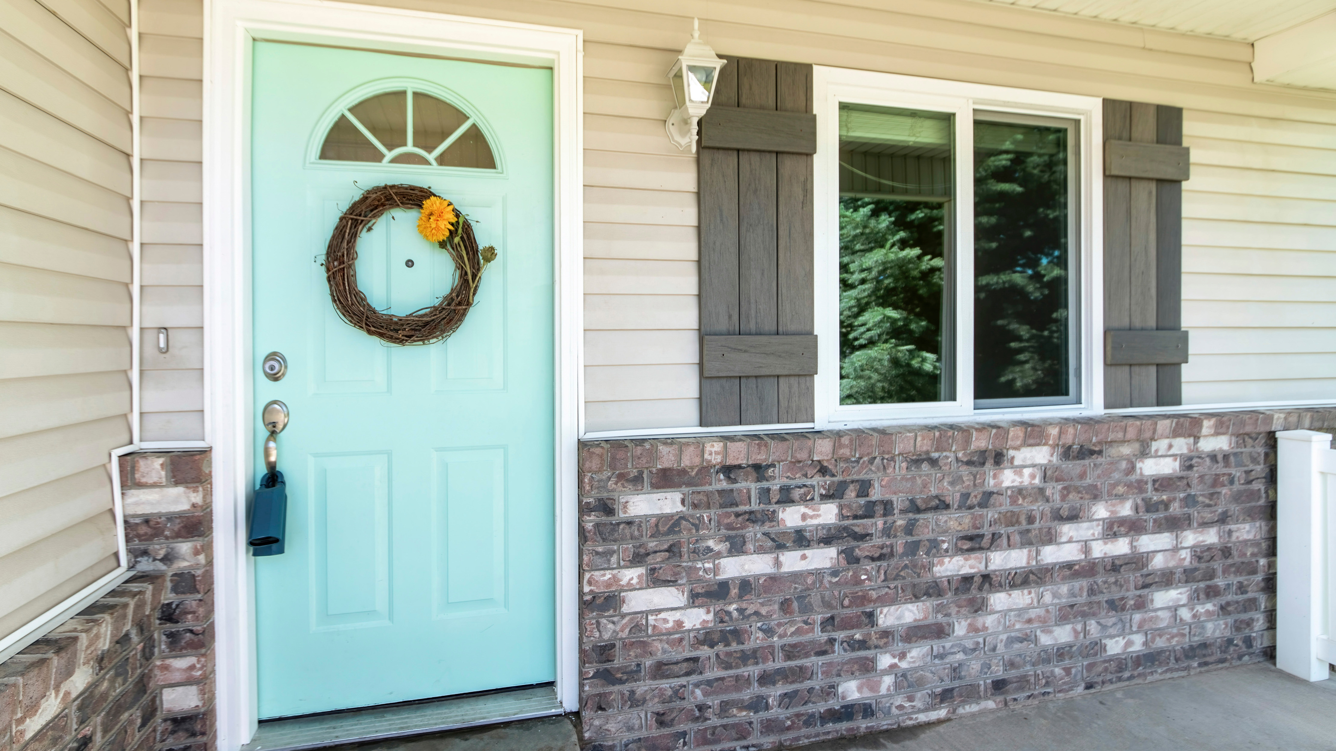A mint green front door with a wreath and vinyl windows in a home exterior.
