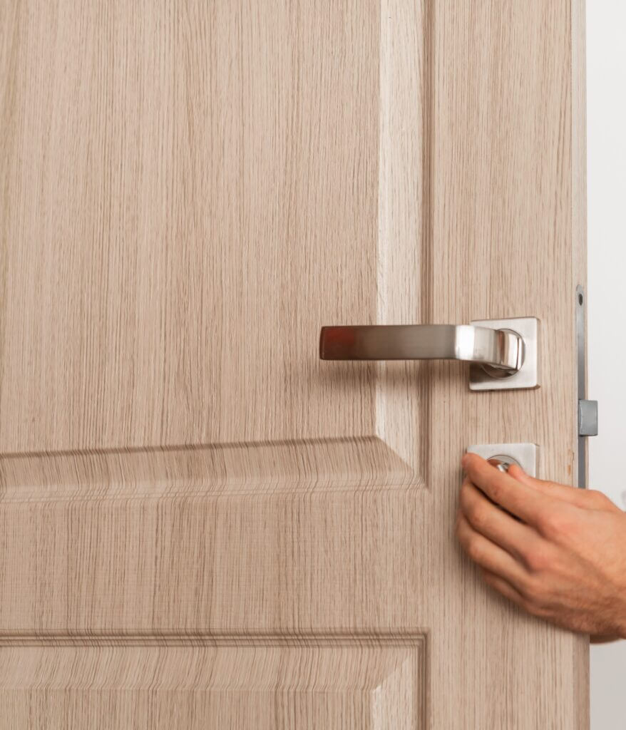 Hand engaging a modern door handle on a wooden exterior door.