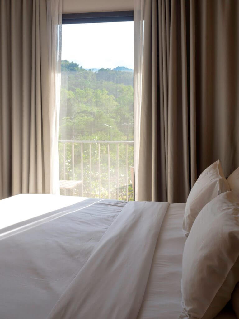 Thermal insulated curtains in a soft beige color, blocking sunlight from a large bedroom window.