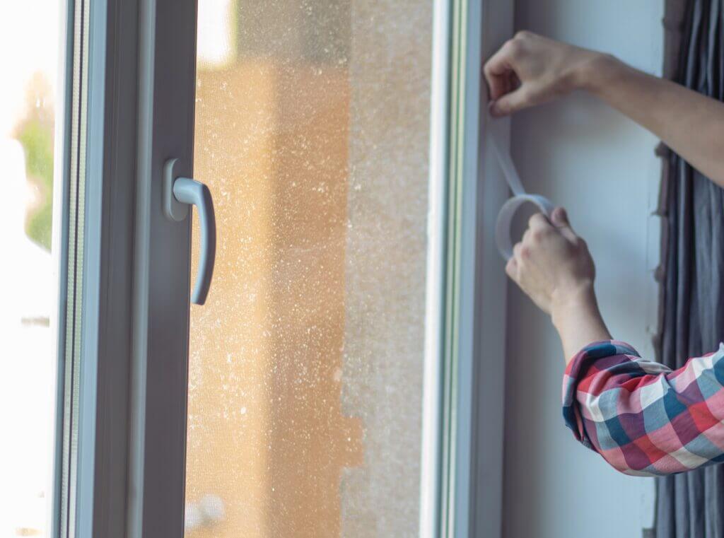 Close-up of a hand applying adhesive weather stripping to a window frame.