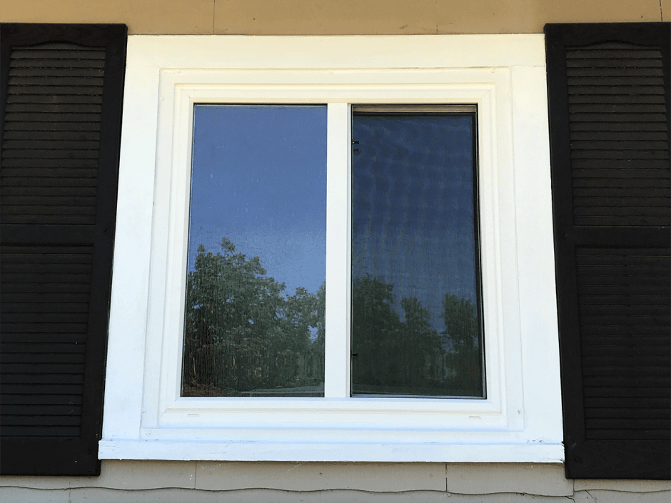 Newly installed modern window with white trim and black shutters on a yellow house in San Antonio.