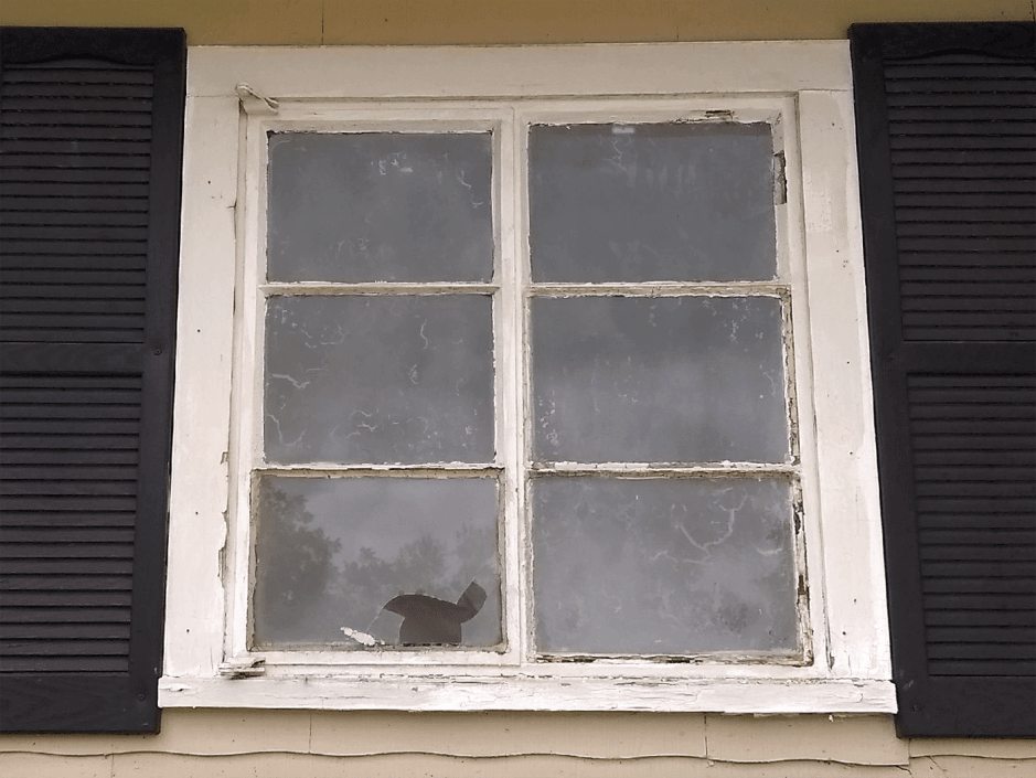 Old, worn-out window with peeling paint and black shutters on a yellow house in San Antonio.
