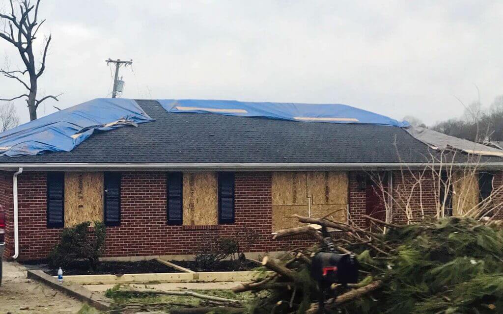 Damaged house with a tarped roof and boarded up windows following a severe storm.