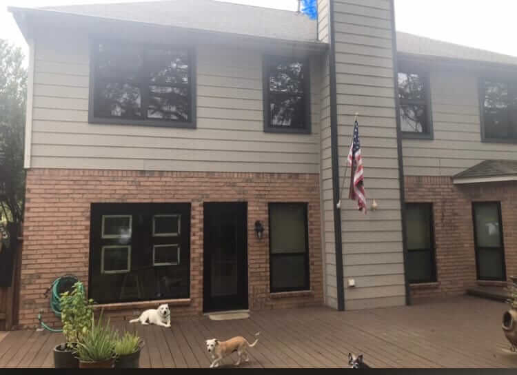 After renovation: Updated two-story home with modern windows and an American flag, dogs playing on the deck in San Antonio.
