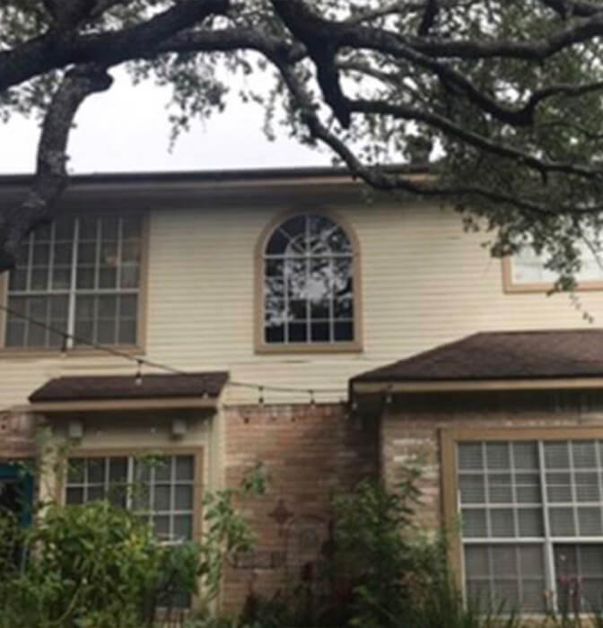 Before renovation: Two-story home in San Antonio with aged windows and overgrown foliage.