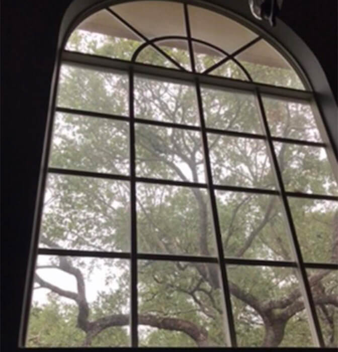 Before renovation: Large arched window with grid design offering a view of lush trees in San Antonio.