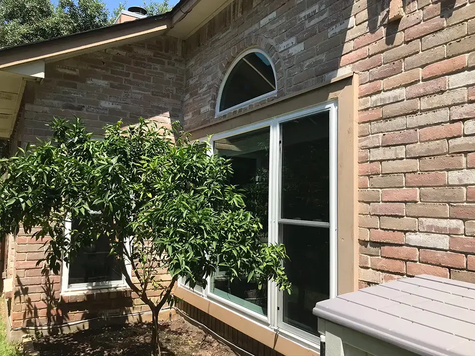 After renovation: Modern, energy-efficient windows installed in a brick house, with trimmed shrubbery enhancing visibility in San Antonio.