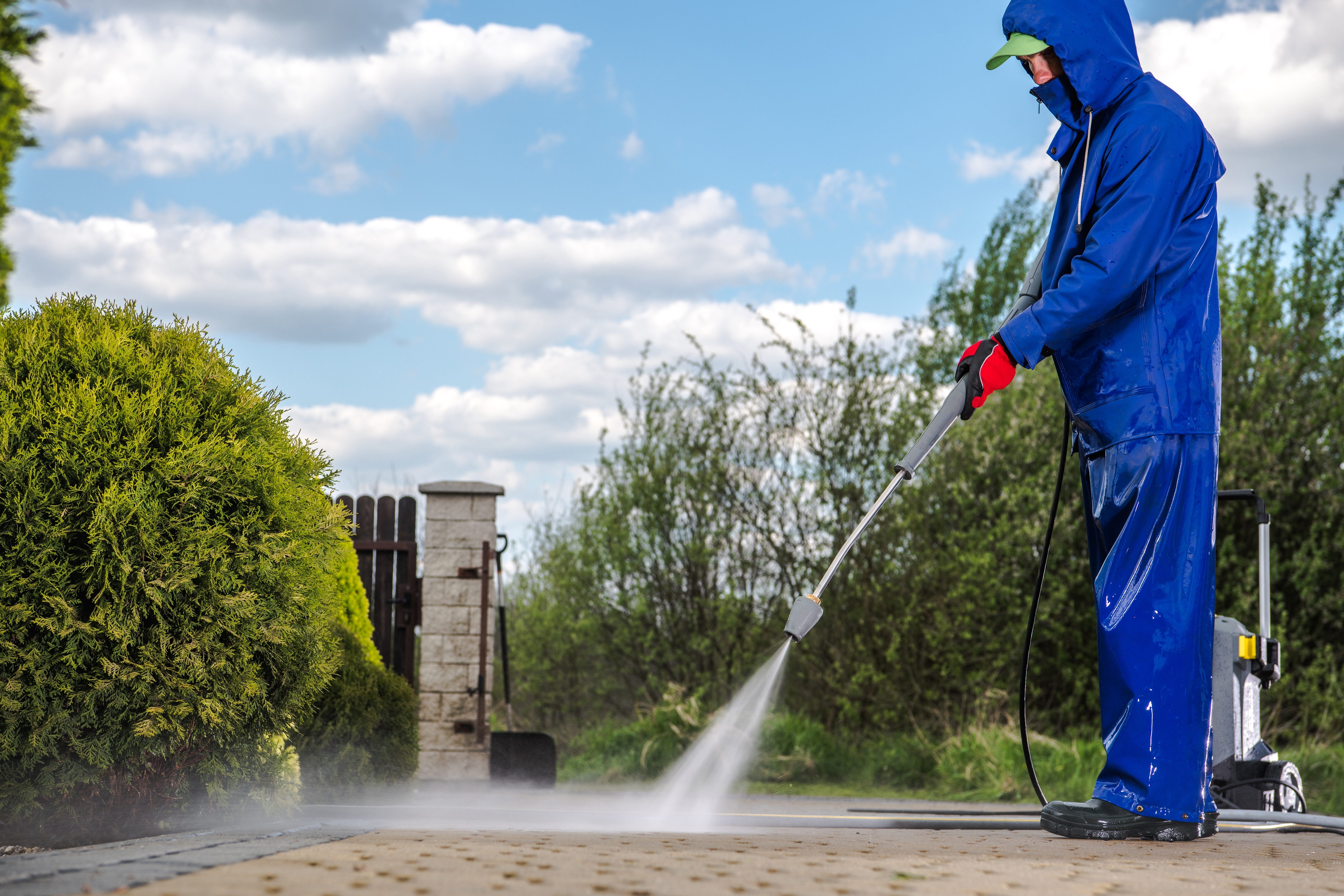 A person in a blue rain suit power washing a driveway, enhancing the home’s curb appeal.
