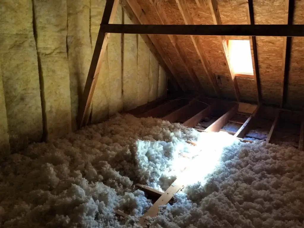 Insulated attic with wooden beams and a small window.