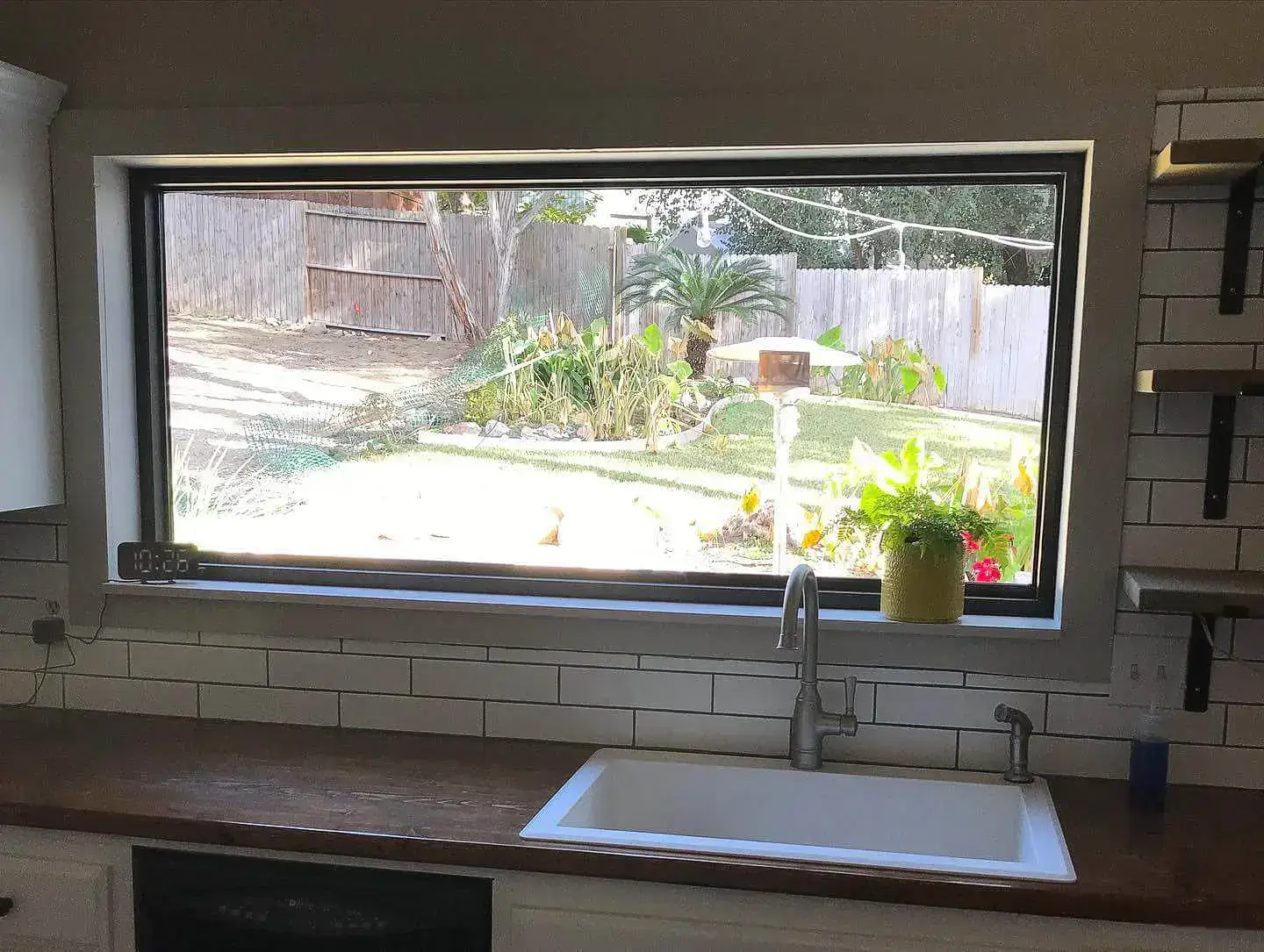 Kitchen view through a large horizontal window showcasing a beautifully landscaped backyard in Corpus Christi.