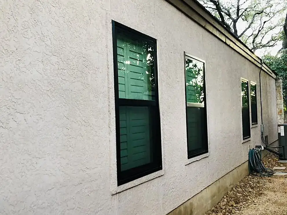 Energy-efficient green shutter windows installed on textured beige exterior wall in San Antonio.