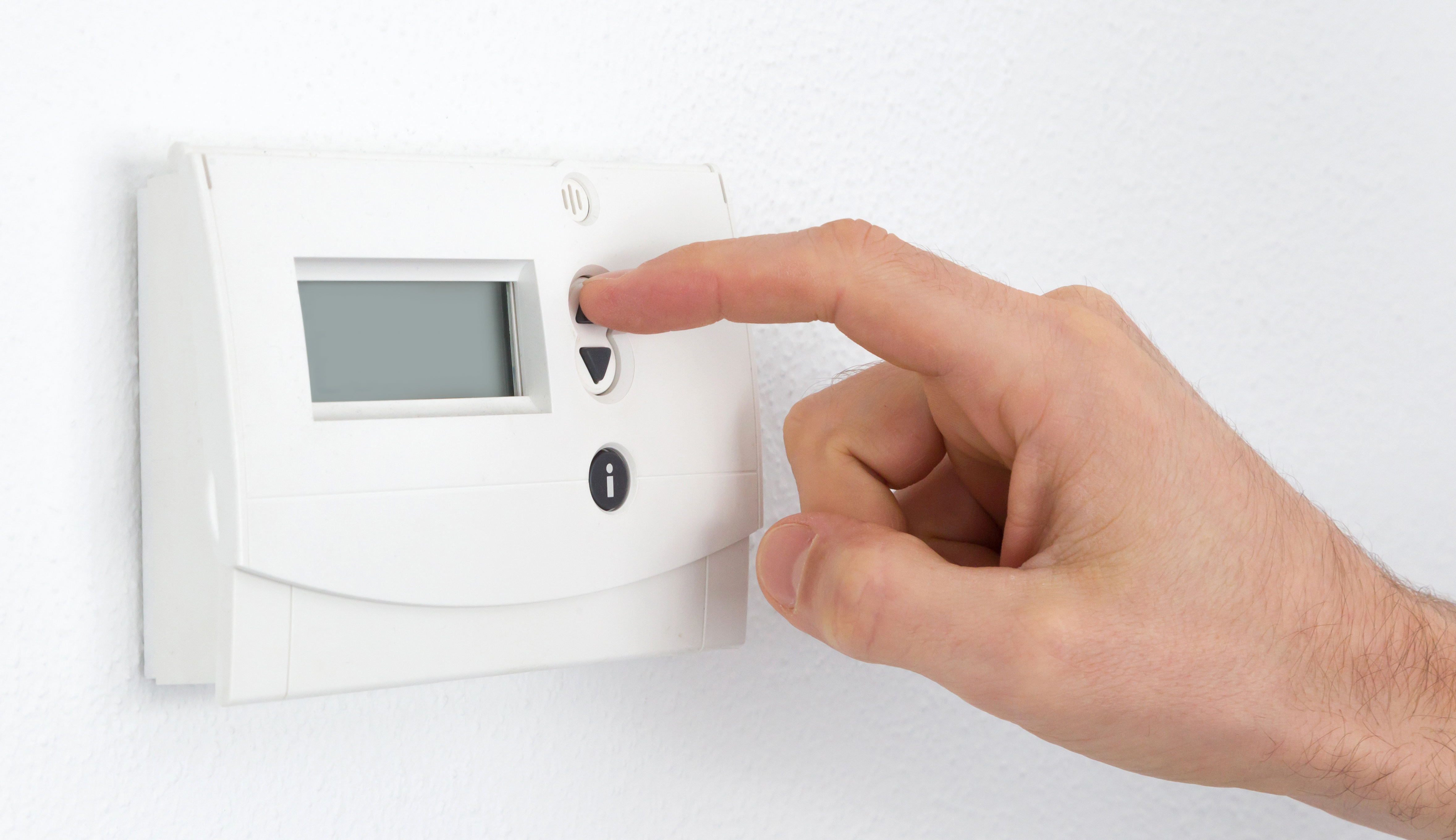 Close-up of a hand adjusting a digital thermostat on a white wall.