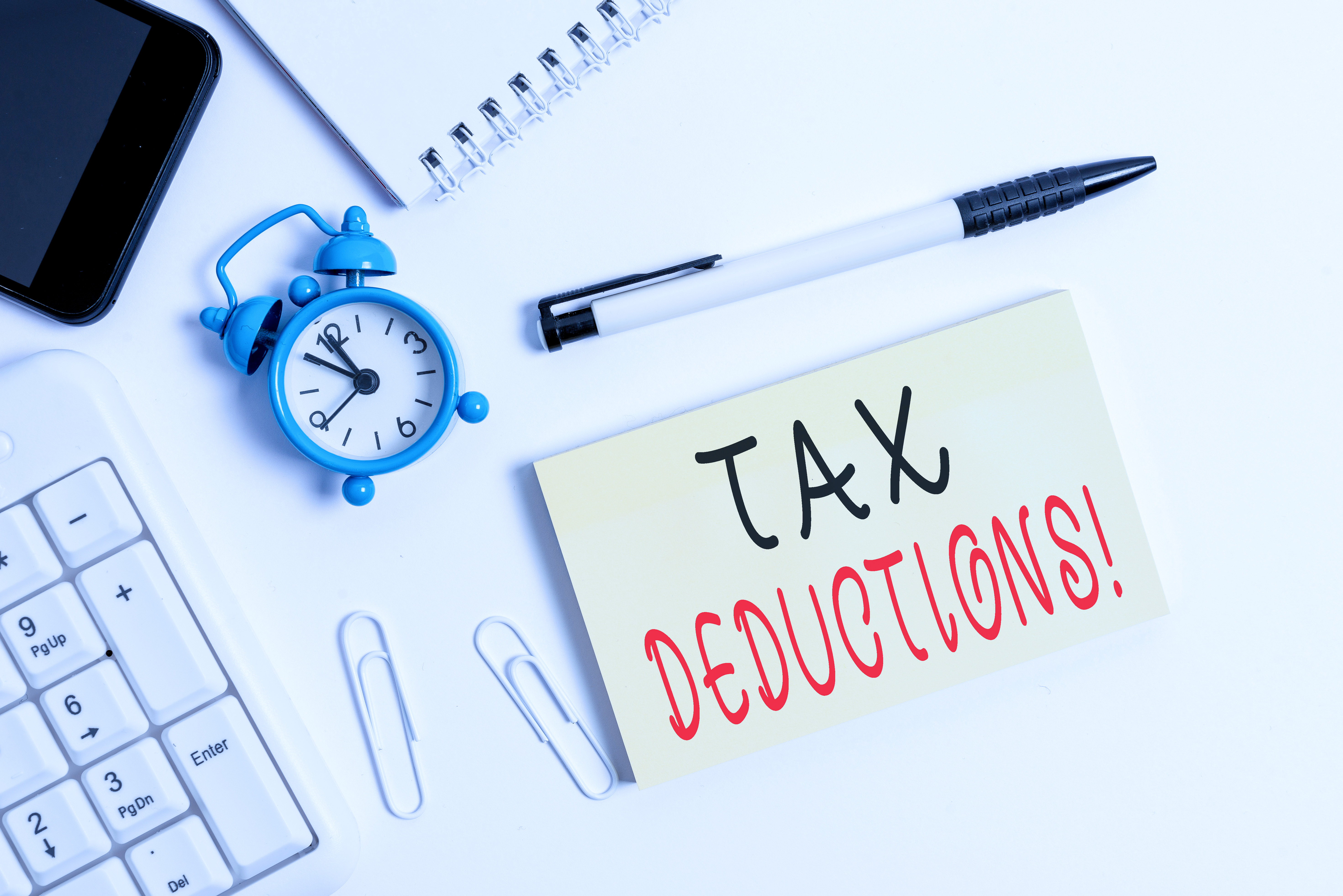 Office desk with a note reading 'TAX DEDUCTIONS!', a calculator, clock, and smartphone.