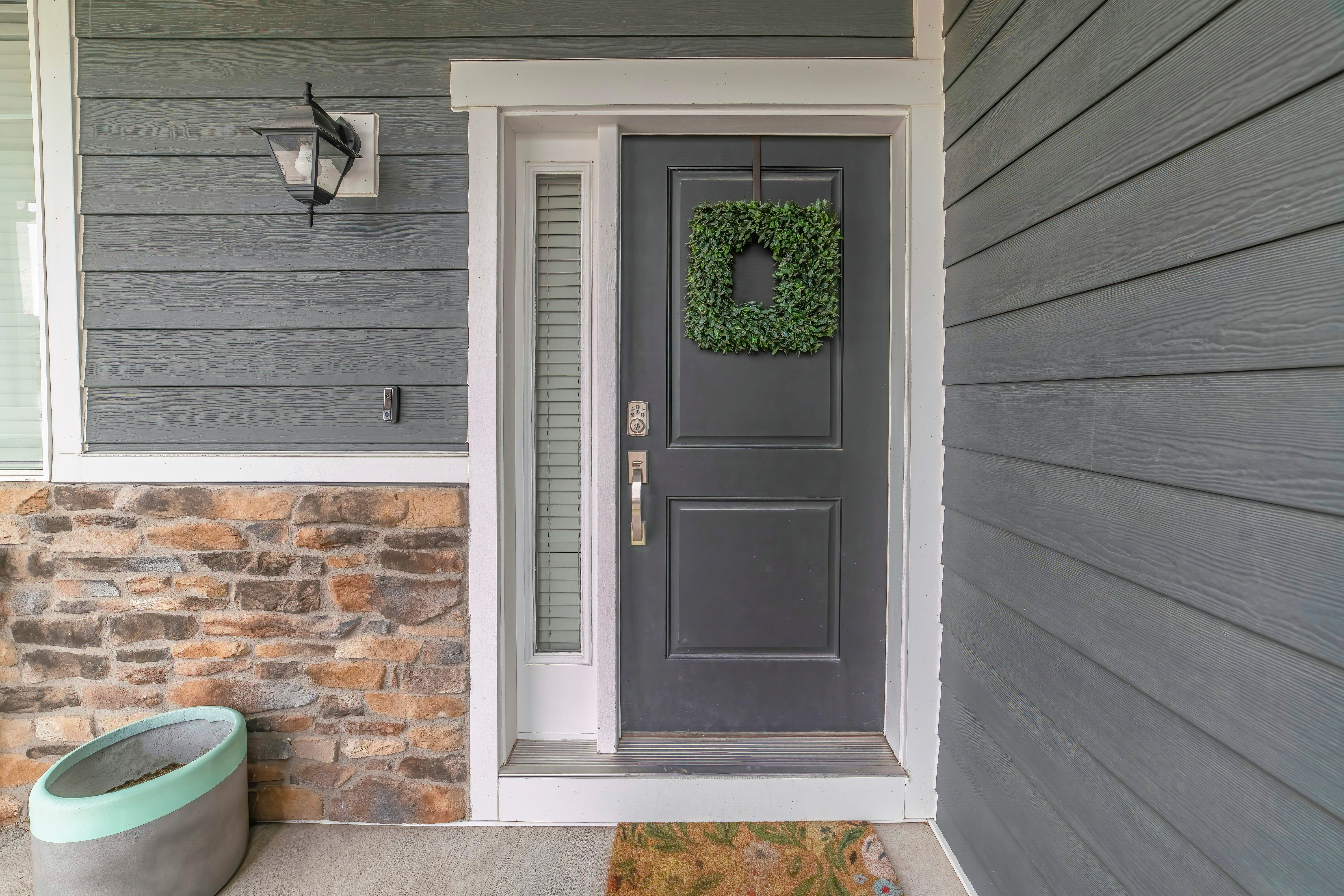 A stylish entryway featuring a dark gray door with a greenery wreath, flanked by a narrow sidelight and stone accents.