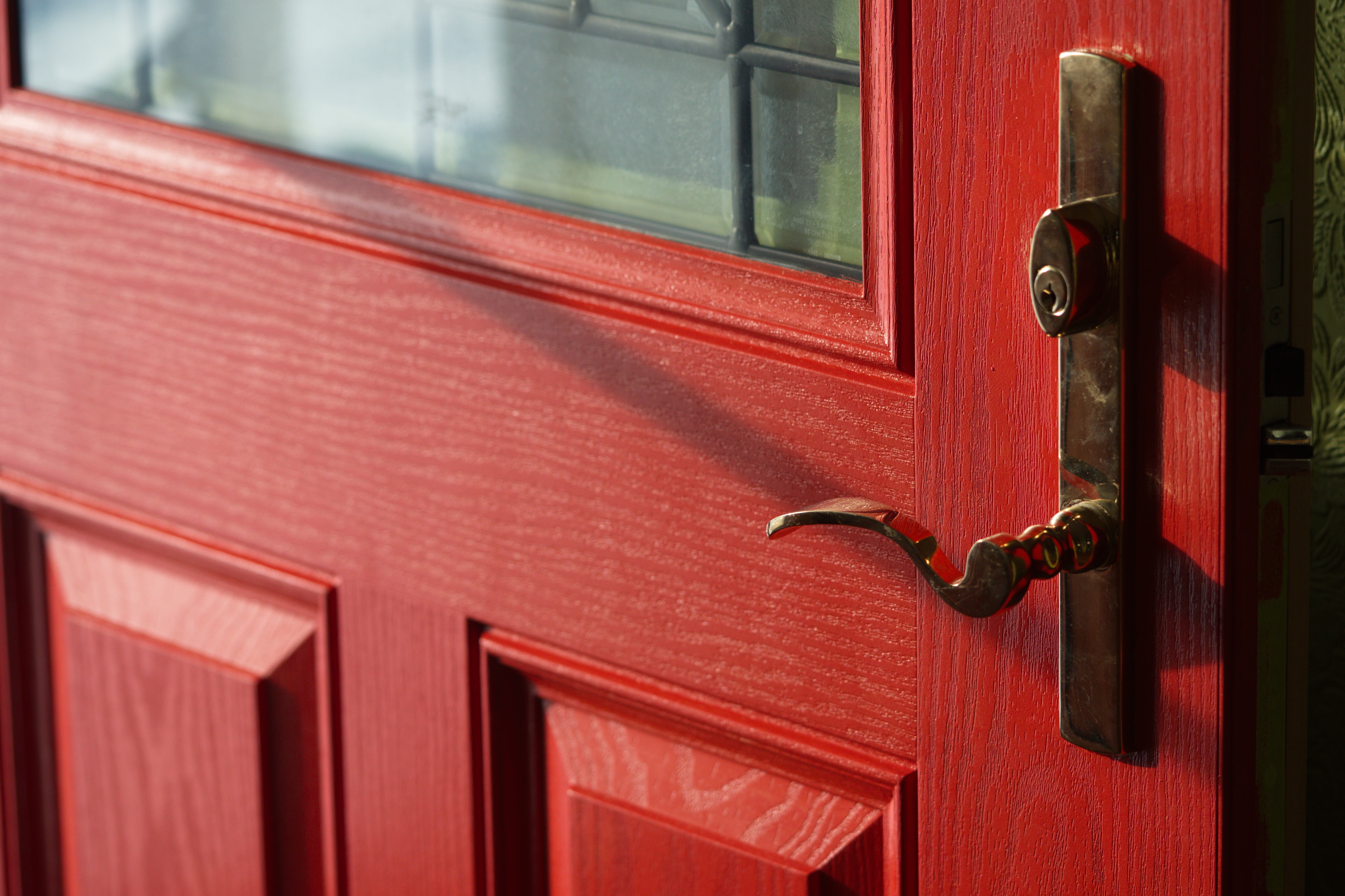 Close-up of a red house door with a handle and lock under natural light.