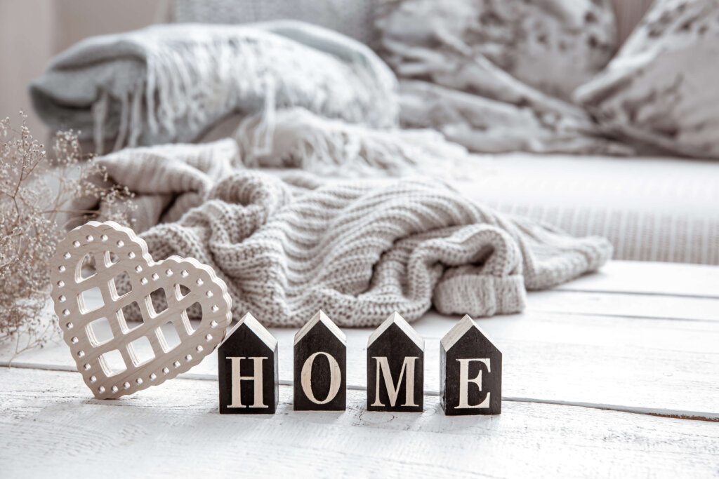 Cozy home scene with 'HOME' spelled out in block letters and a heart-shaped decoration on a wooden table, surrounded by a knitted blanket and cushions.