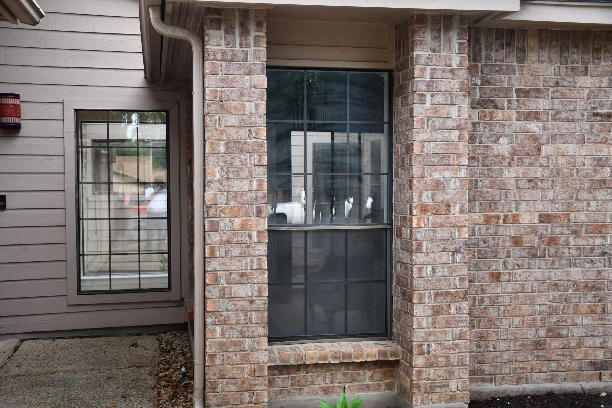Before photo of an old window needing replacement, set in a brick house with gray siding, located in San Antonio, Texas.