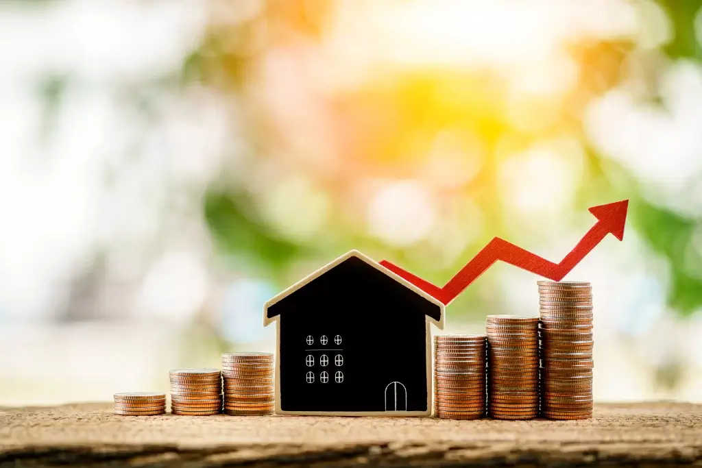 Stacks of coins and a model house with an upward arrow symbolizing increased property value.