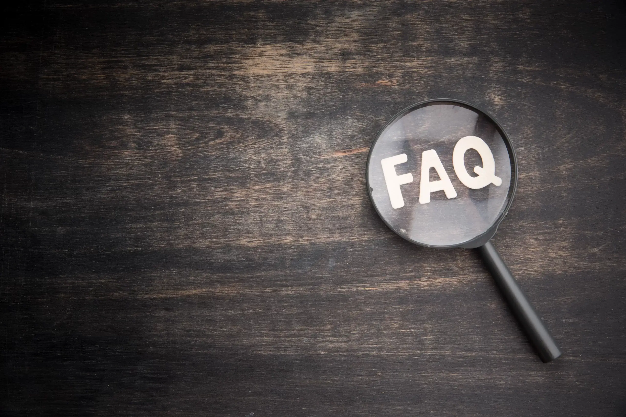 Magnifying glass highlighting the letters FAQ on a wooden background.