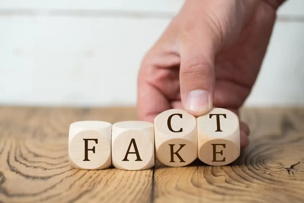 Hand turning a wooden block from 'FAKE' to 'FACT'.