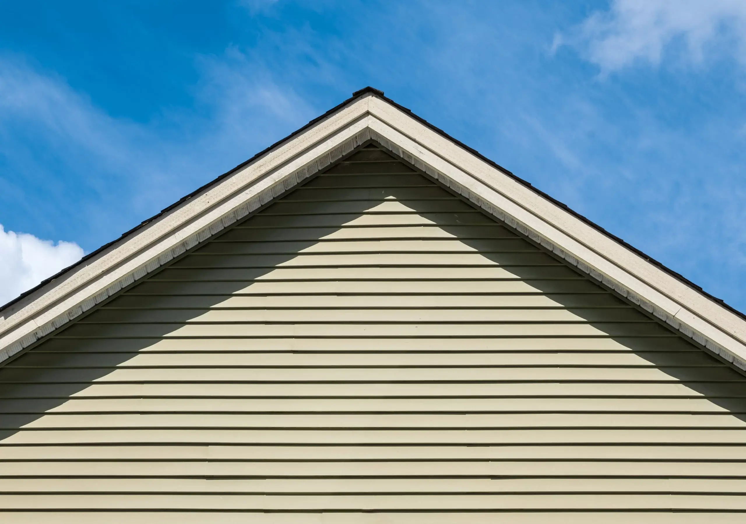 Close-up of a house's vinyl siding against a clear blue sky, showcasing a well-maintained exterior.